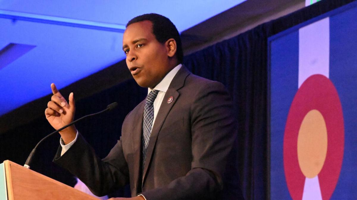 Congressman Joe Neguse stands in front of a podium while he gives a speech at the Colorado Democratic Party midterm watch party. A Colorado state flag is visible in the background. 